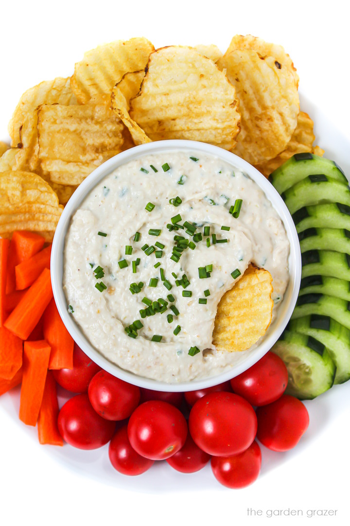 Vegan French onion dip in a white bowl with veggies and chips
