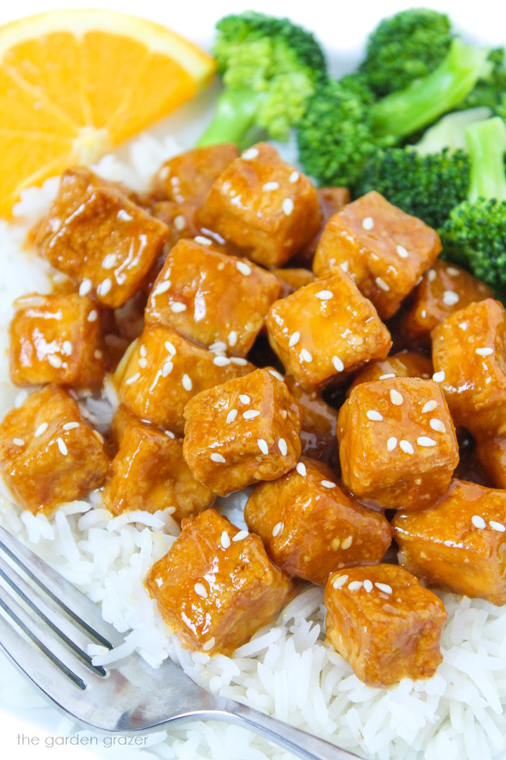 Close up view of orange tofu on top of white rice with broccoli