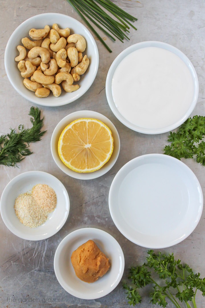 Raw nuts, vinegar, lemon, miso, yogurt, and fresh herb ingredients laid out on a tray