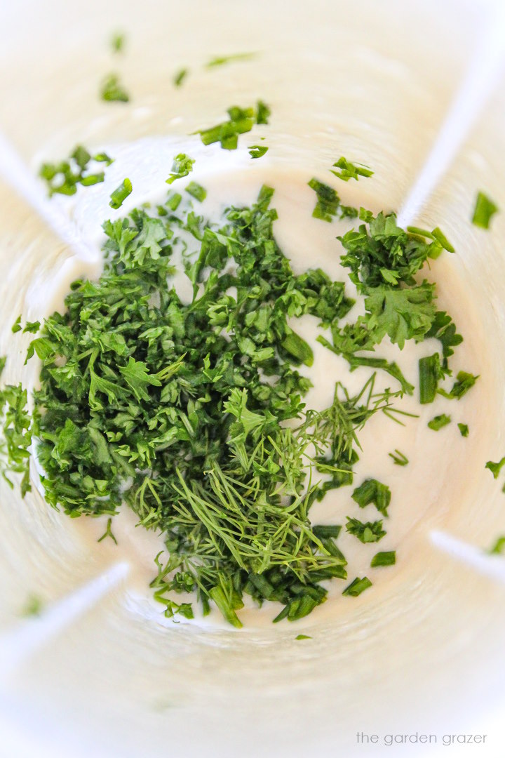 Overhead view of vegan ranch dressing in blender with herbs added