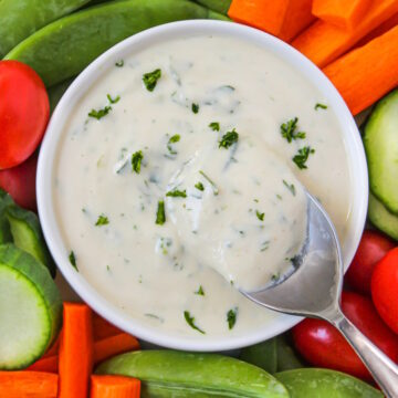 Close up view of vegan ranch dressing in a white bowl with raw veggies for dipping