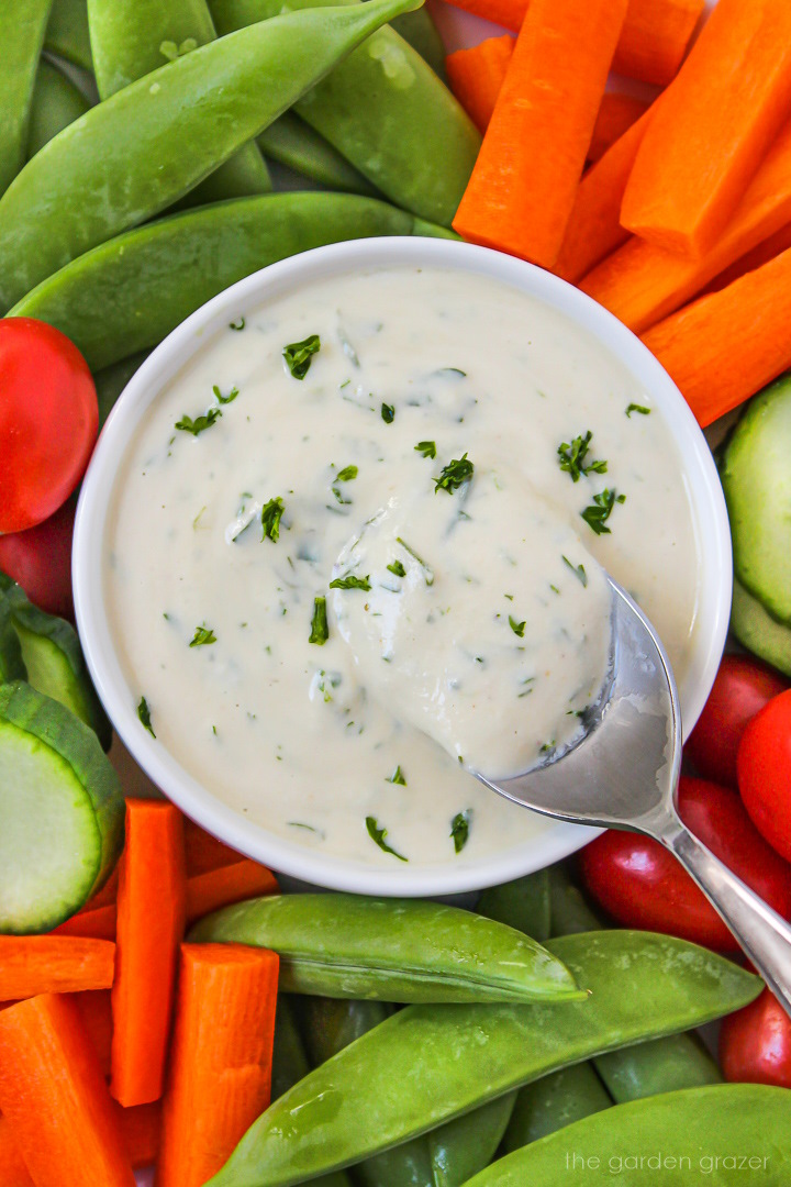 Close up view of vegan ranch dressing in a white bowl with raw veggies for dipping