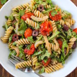 Overhead view of arugula pasta salad in a white bowl on a wooden table