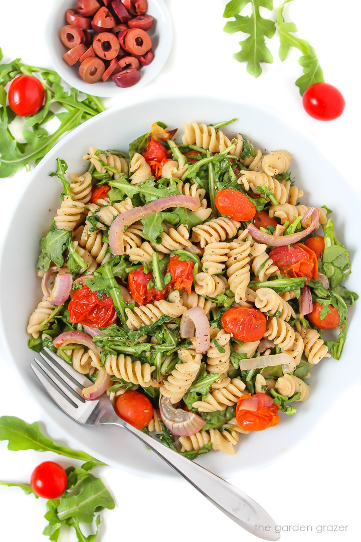 Vegan arugula pasta salad in a white bowl with fork