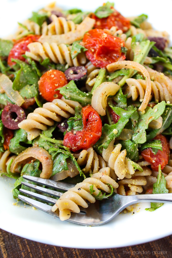 Close up view of arugula pasta salad on a white serving plate with fork