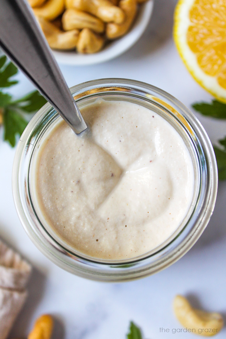 Overhead view of vegan cashew mayo in a small glass jar with serving spoon