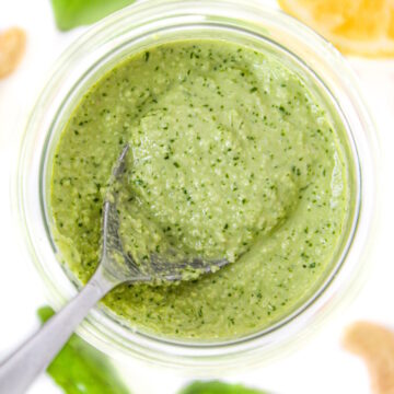 Overhead view of spoon scooping out vegan cashew pesto from a small glass jar