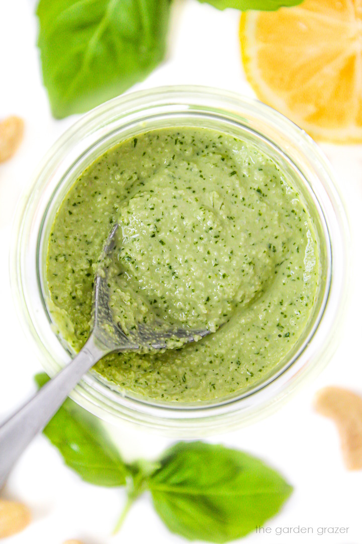 Overhead view of spoon scooping out vegan cashew pesto from a small glass jar