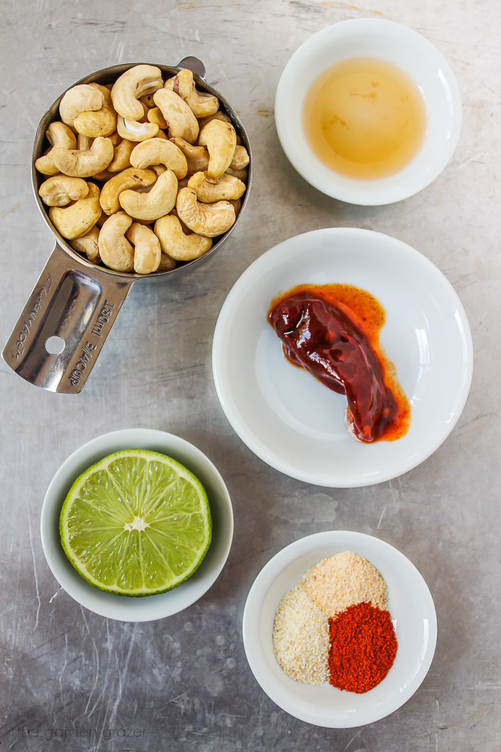 Raw cashews, lime, vinegar, and dry spice ingredients laid out on a table