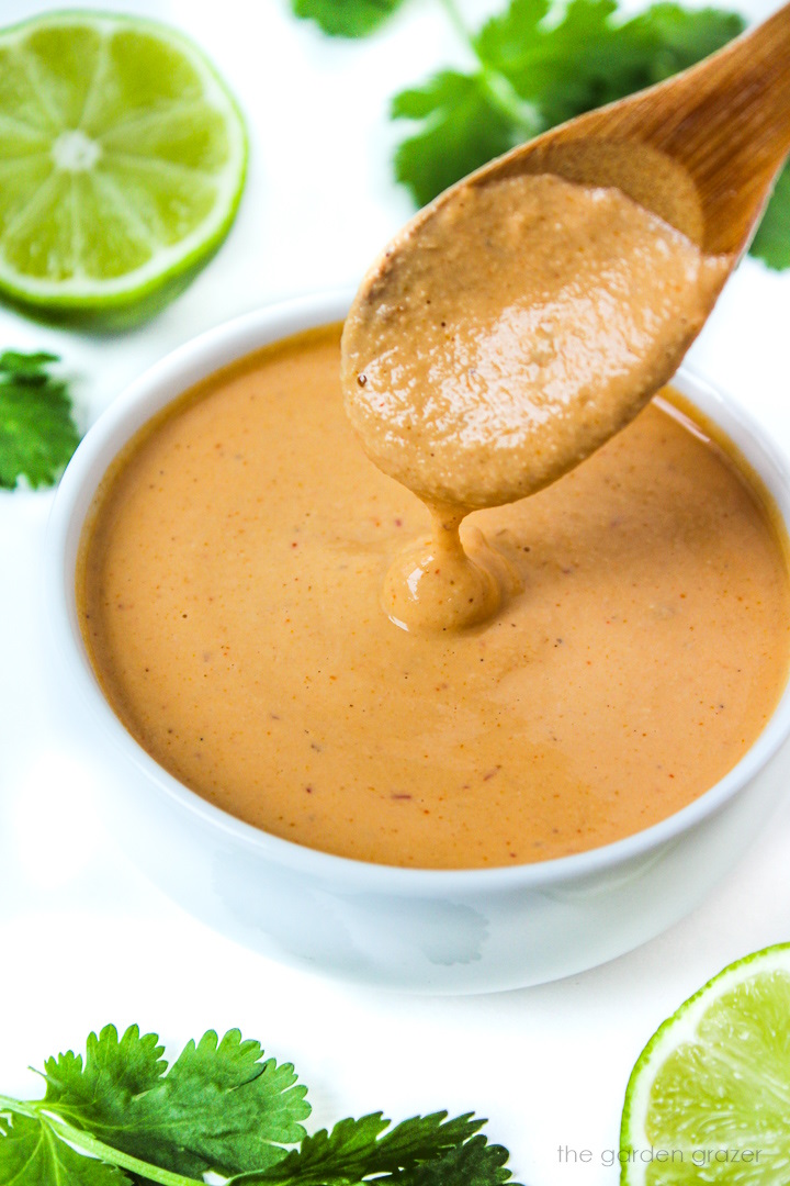 Wooden spoon lifting up vegan chipotle crema from a small white bowl