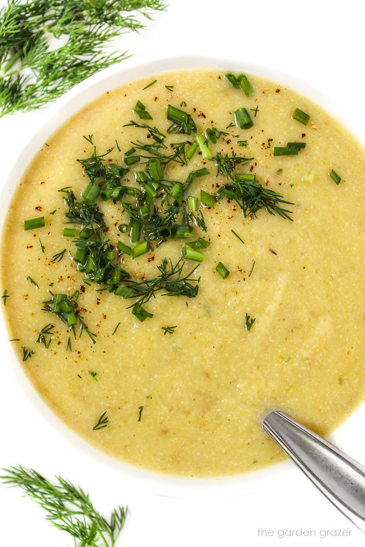 Overhead view of vegan potato leek soup garnished with fresh herbs in a white bowl