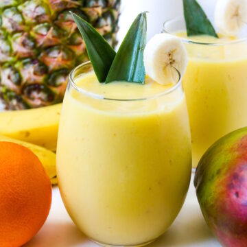 Two glasses of creamy mango pineapple smoothie garnished with a banana slice