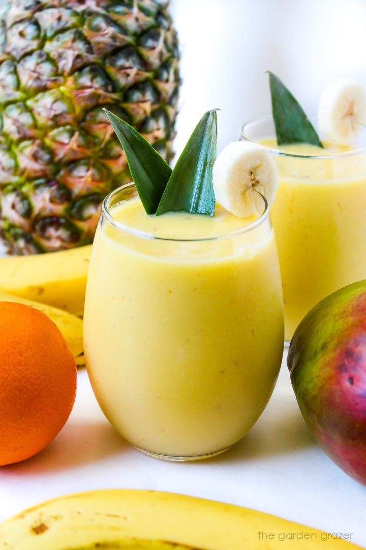 Two glasses of creamy mango pineapple smoothie garnished with a banana slice