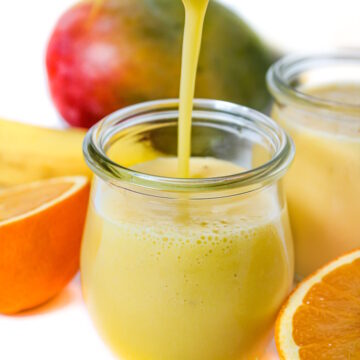 Pouring mango pineapple smoothie into a small glass jar
