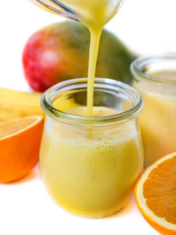 Pouring mango pineapple smoothie into a small glass jar