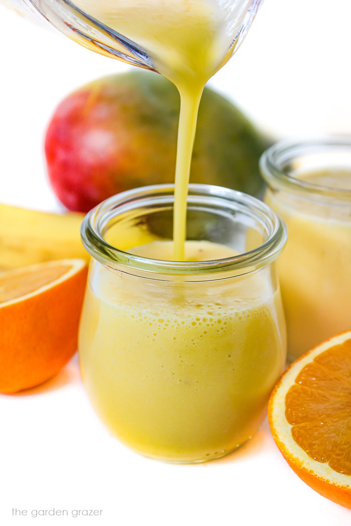 Pouring mango pineapple smoothie into a small glass jar