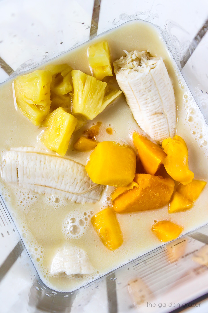 Overhead view of preparing fruit, juice, and milk ingredients in a blender before blending
