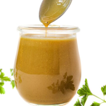 Spoon lifting out maple Dijon dressing from a small glass jar