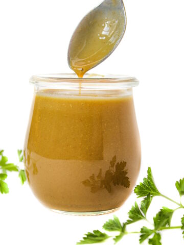 Spoon lifting out maple Dijon dressing from a small glass jar