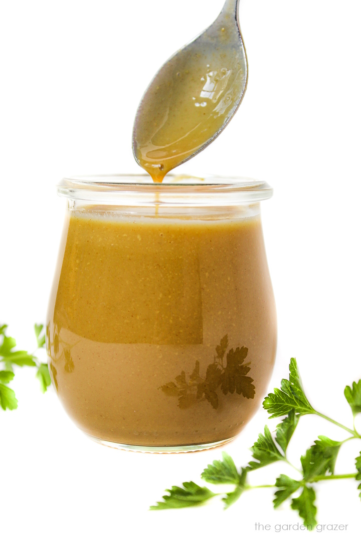 Spoon lifting out maple Dijon dressing (vegan honey mustard) from a small glass jar