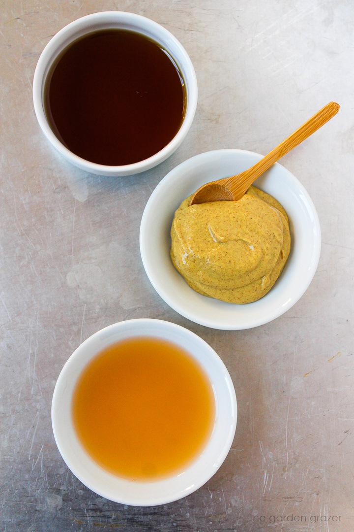 Mustard, maple syrup, and apple cider vinegar ingredients laid out in bowls on a metal tray