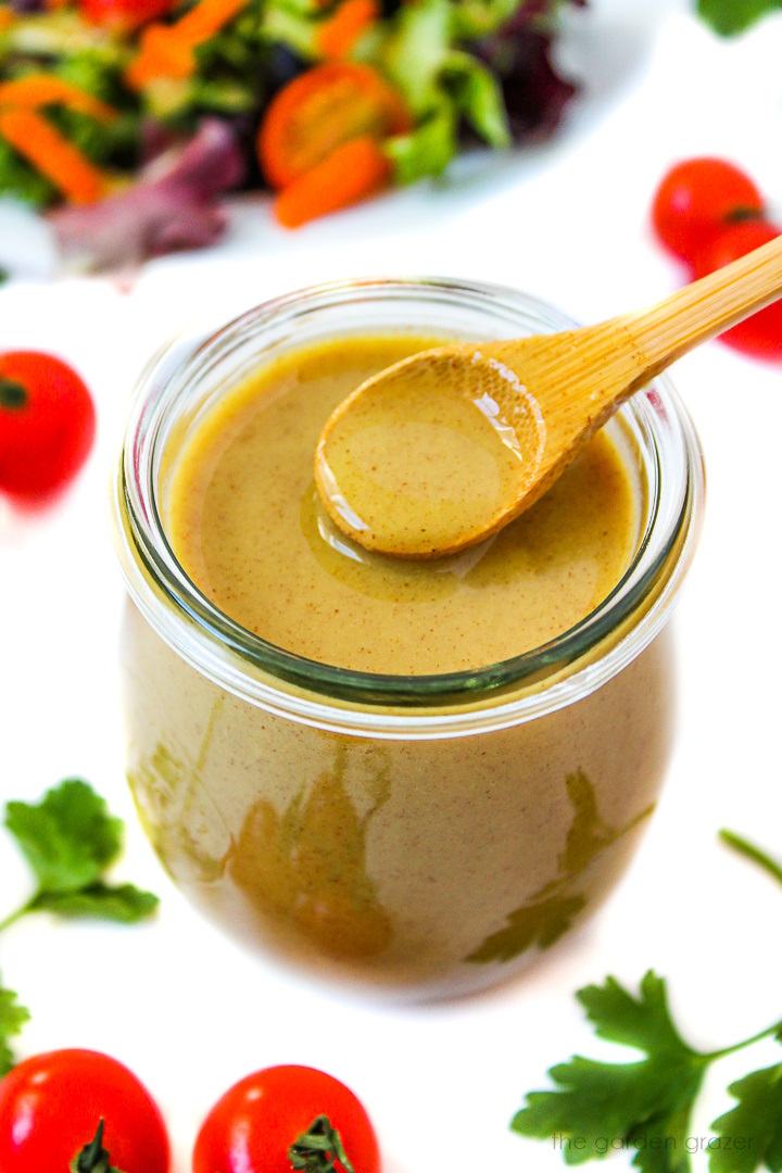 A wooden spoon lifting up maple Dijon dressing from a small glass jar