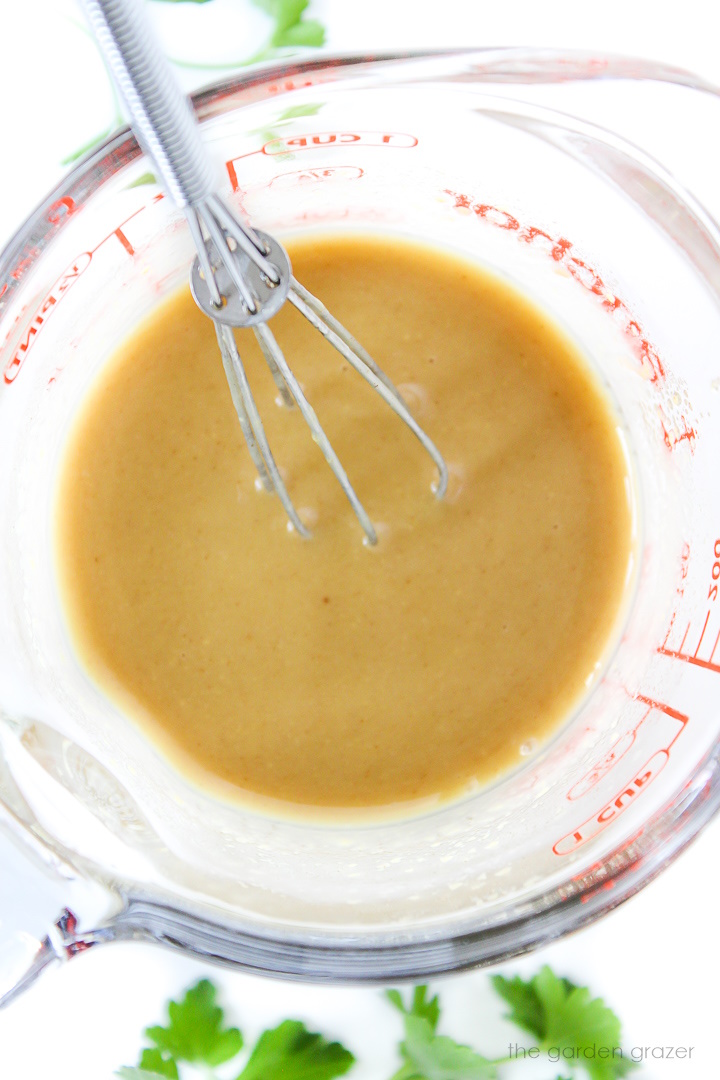 Whisking together maple Dijon dressing (vegan honey mustard) in a small glass measuring cup
