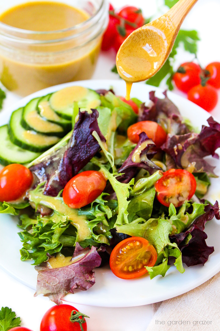 Maple Dijon Dressing being poured on a simple mixed greens salad