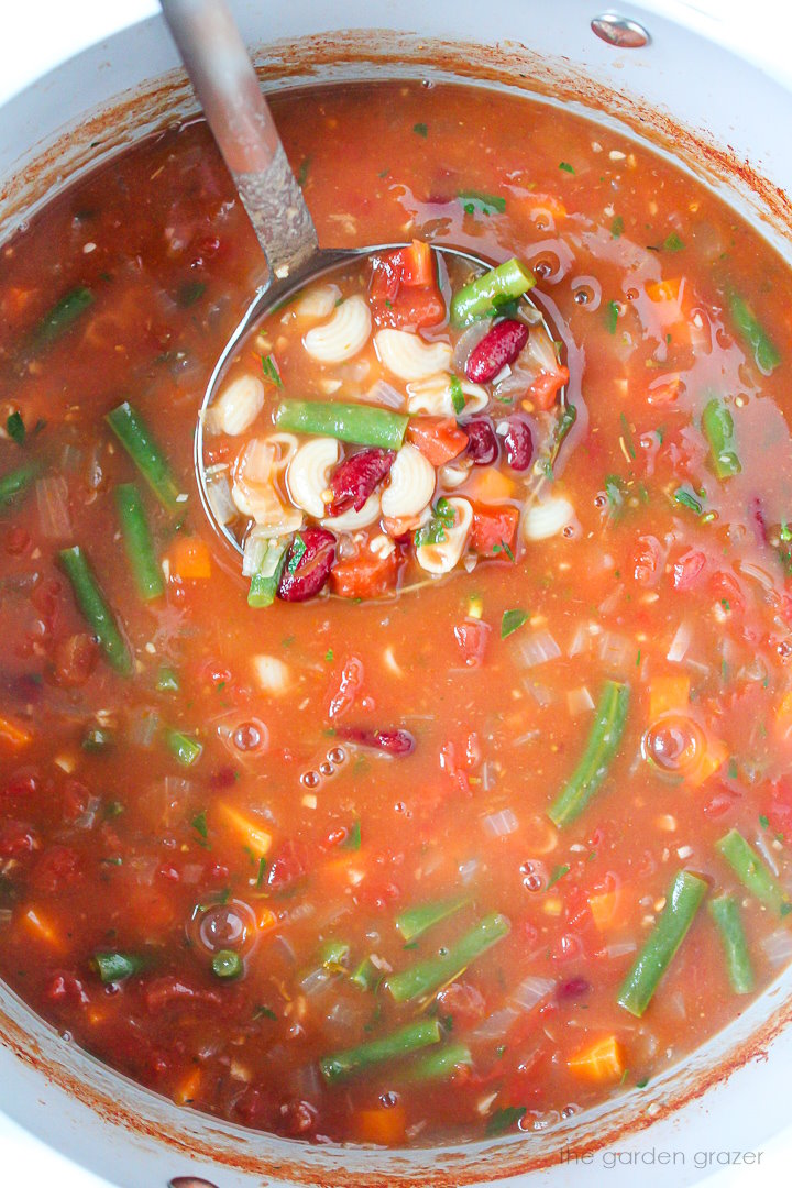 Ladle scooping out vegan minestrone soup from a pot