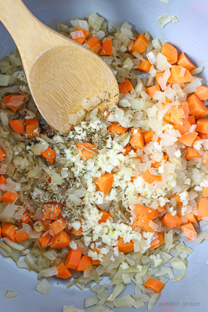 Onions, carrot, garlic, and seasonings cooking in a pot with wooden stirring spoon