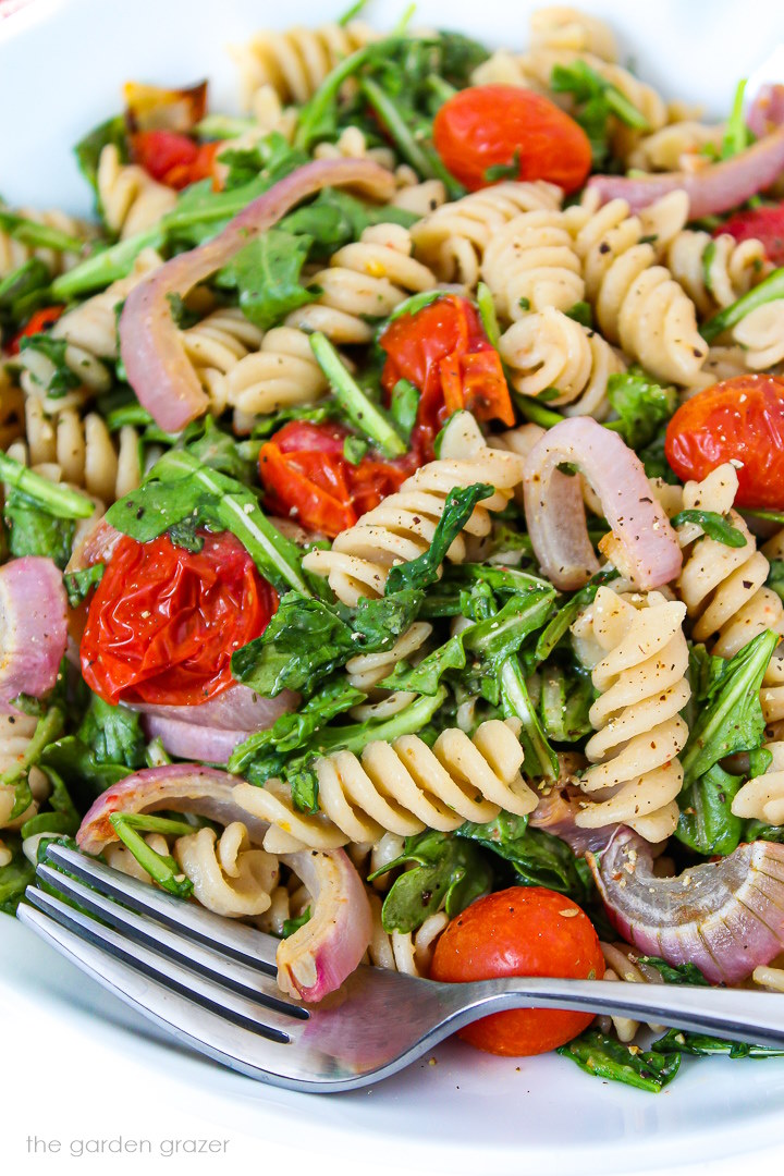 Close up view of arugula pasta salad with roasted tomatoes on a white plate