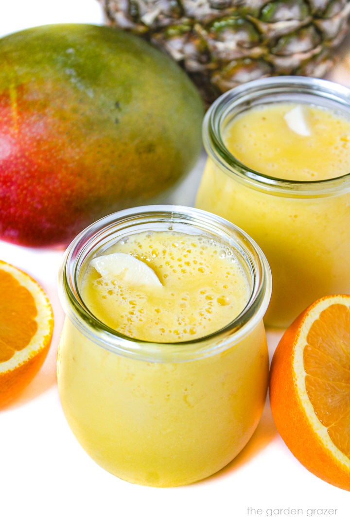 Two glasses of mango pineapple smoothie surrounded by fresh fruit