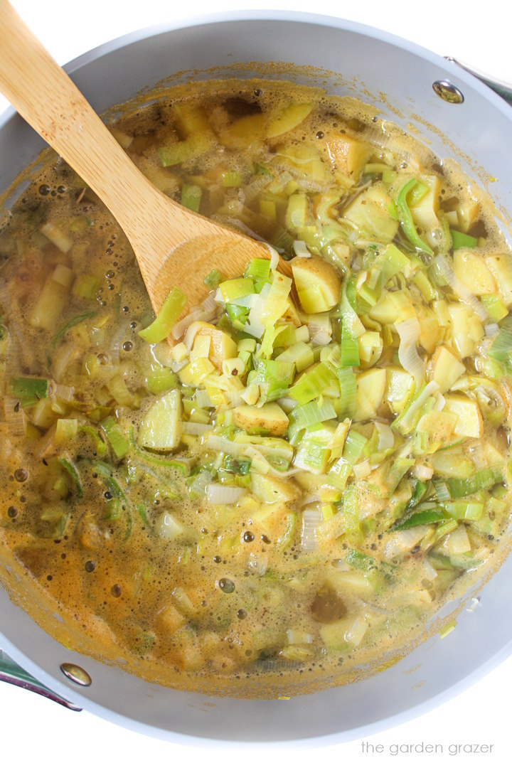 Overhead view of soup cooking in a stockpot with wooden stirring spoon
