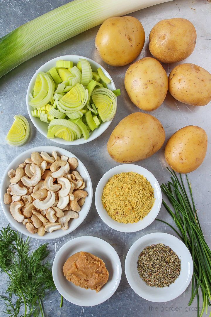 Leeks, gold potatoes, cashews, miso, nutritional yeast, and fresh herb ingredients laid out on a metal tray