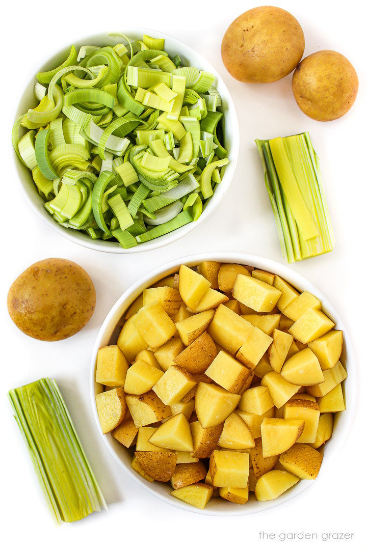 Sliced fresh leeks and diced gold potato ingredients in white bowls