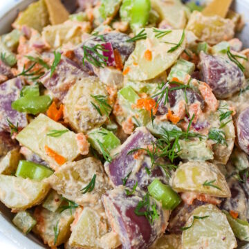 Close up view of vegan potato salad in a white bowl with bamboo serving spoons