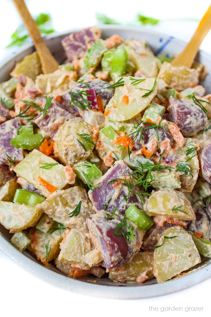 Close up view of vegan potato salad in a white bowl with bamboo serving spoons