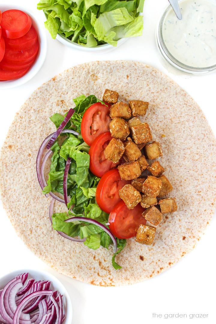 Open-faced tofu wrap on a tortilla with lettuce, tomato, and onion