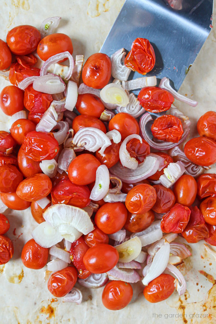 Roasted grape tomatoes and sliced shallots on a tray with metal spatula