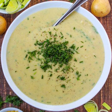 Vegan potato leek soup in a white bowl topped with fresh dill and chives