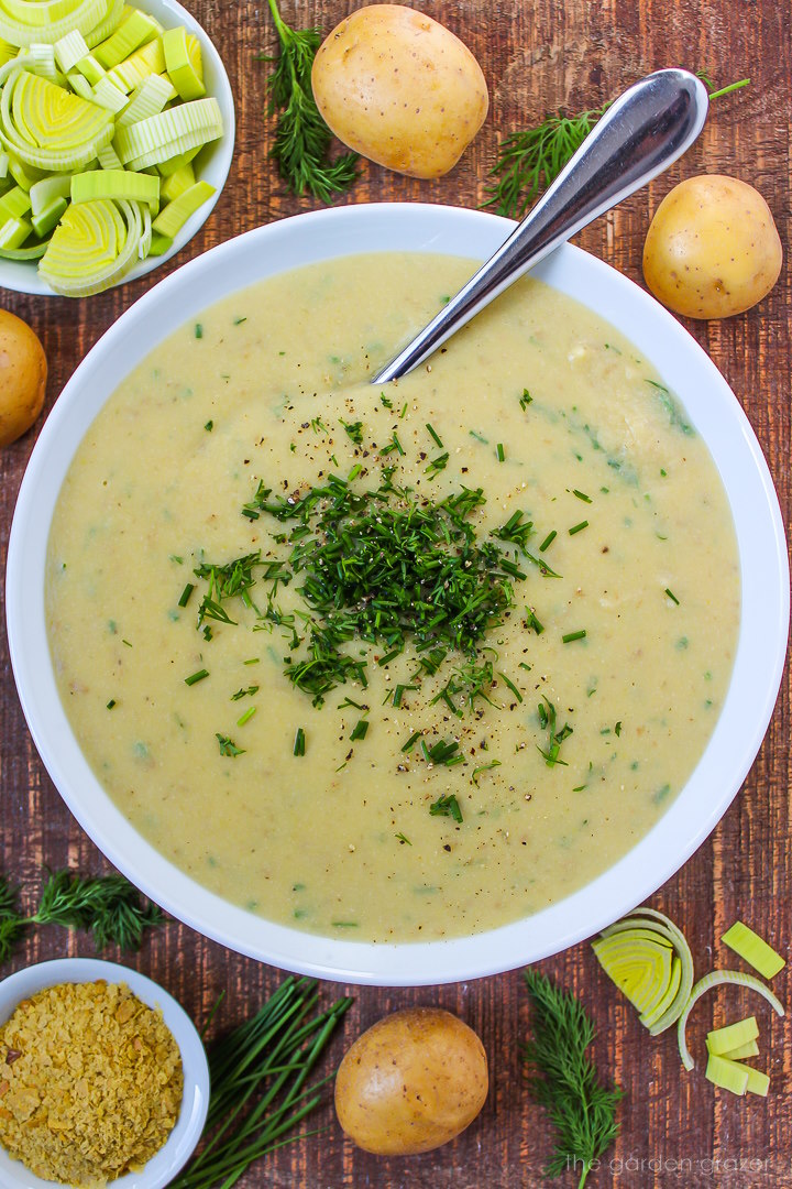 Vegan potato leek soup in a white bowl topped with fresh dill and chives