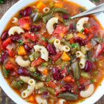 Vegan minestrone soup in a white bowl with serving spoon on a wooden table