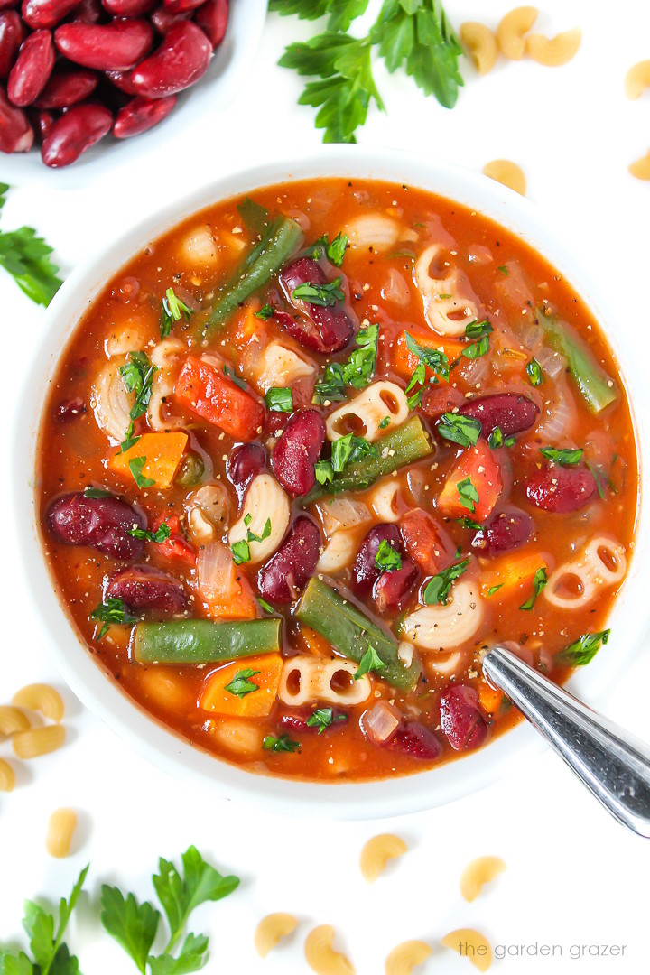 Overhead view of vegan minestrone soup in a white bowl with spoon
