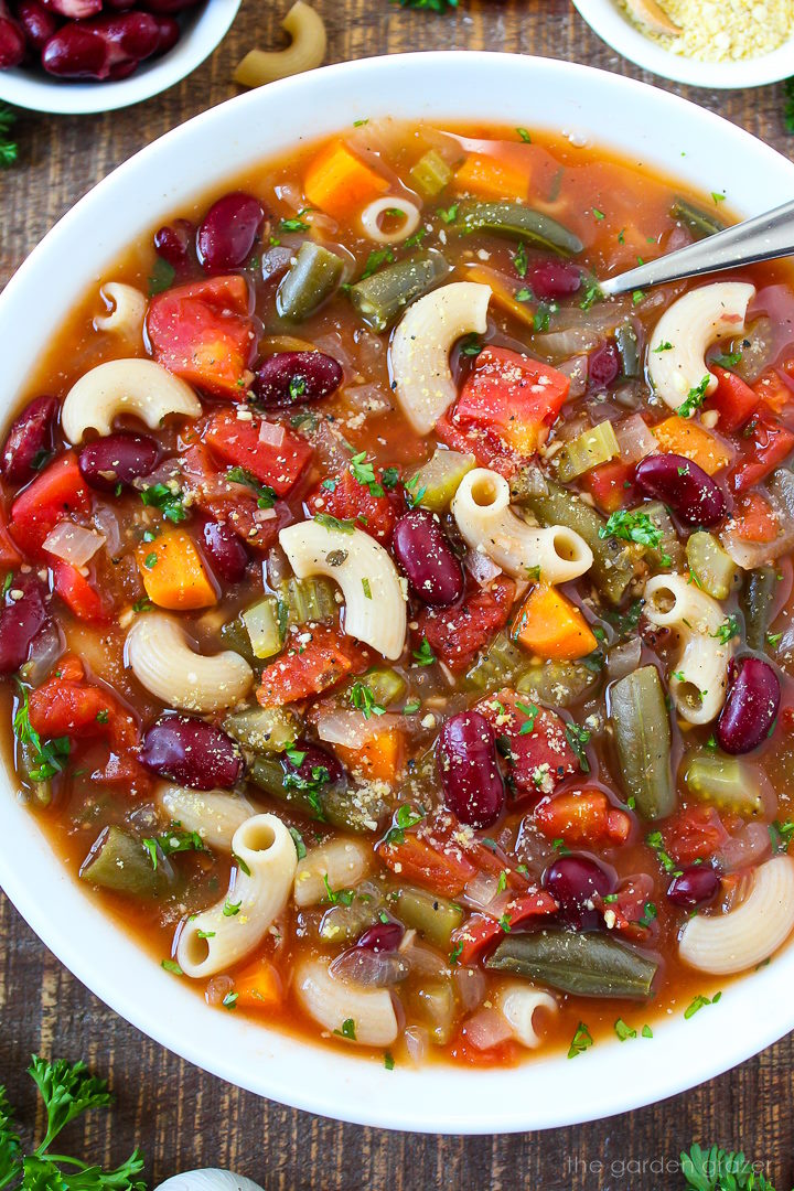 Close up view of vegan minestrone soup in a white serving bowl with spoon