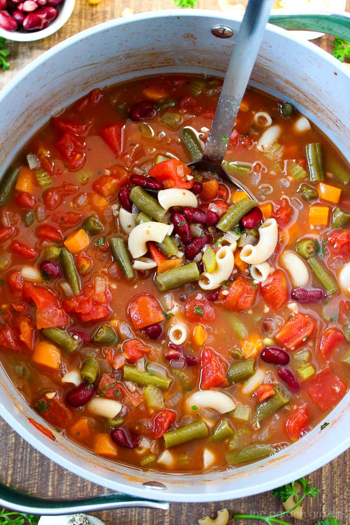 Overhead view of vegan minestrone soup cooking in a large pot with metal ladle