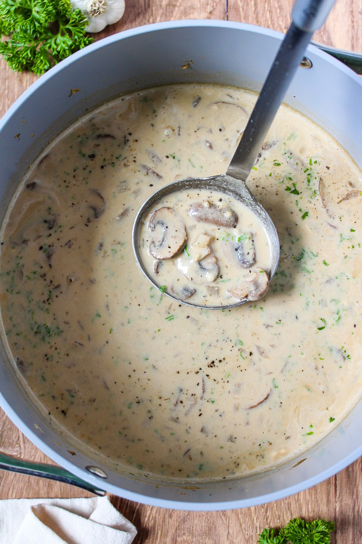 A metal ladle lifting up vegan mushroom soup from a pot after it cooks