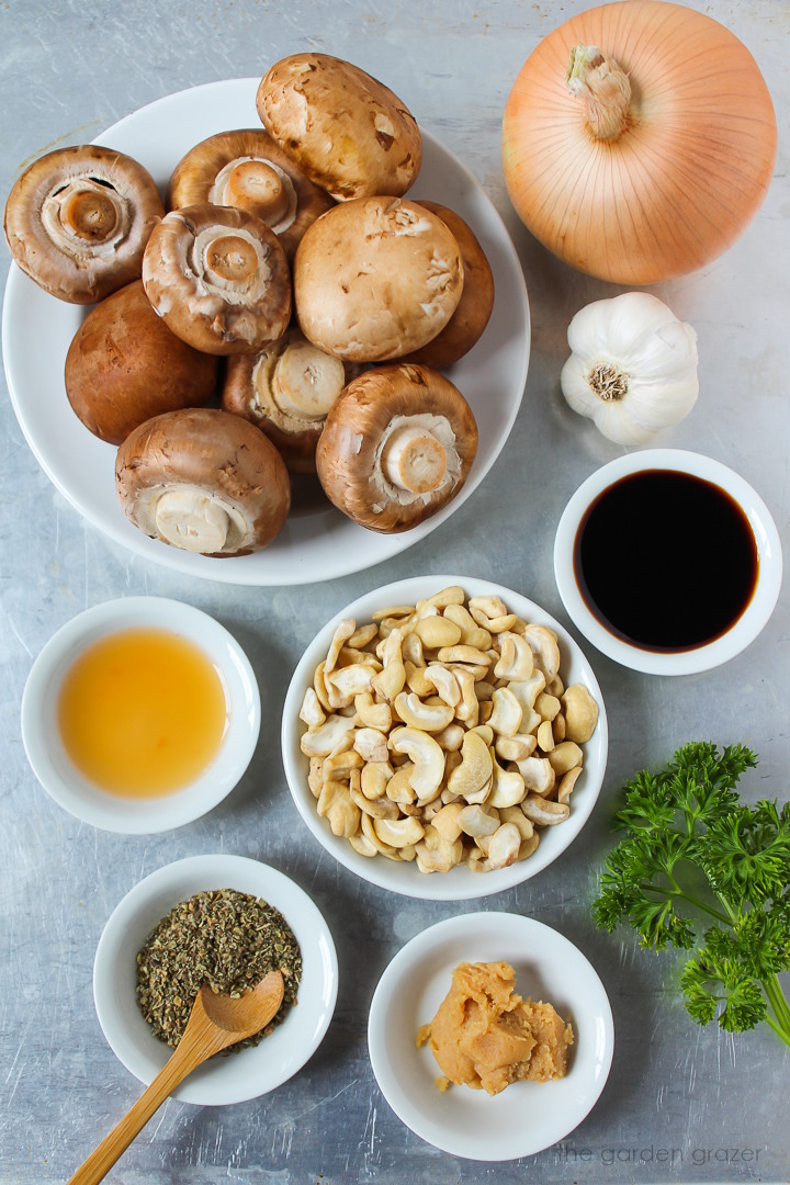 Cremini mushrooms, onion, garlic, raw cashews, tamari, miso, and seasoning ingredients laid out on a metal tray