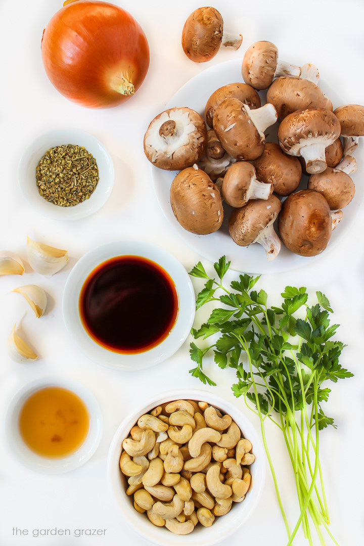 Fresh creminis, onion, cashews, tamari, and herb ingredients laid out on a white table