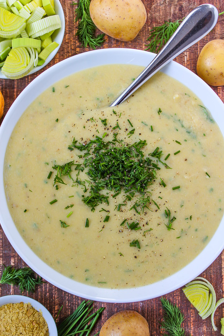 Close-up view of vegan potato leek soup in a white bowl with serving spoon