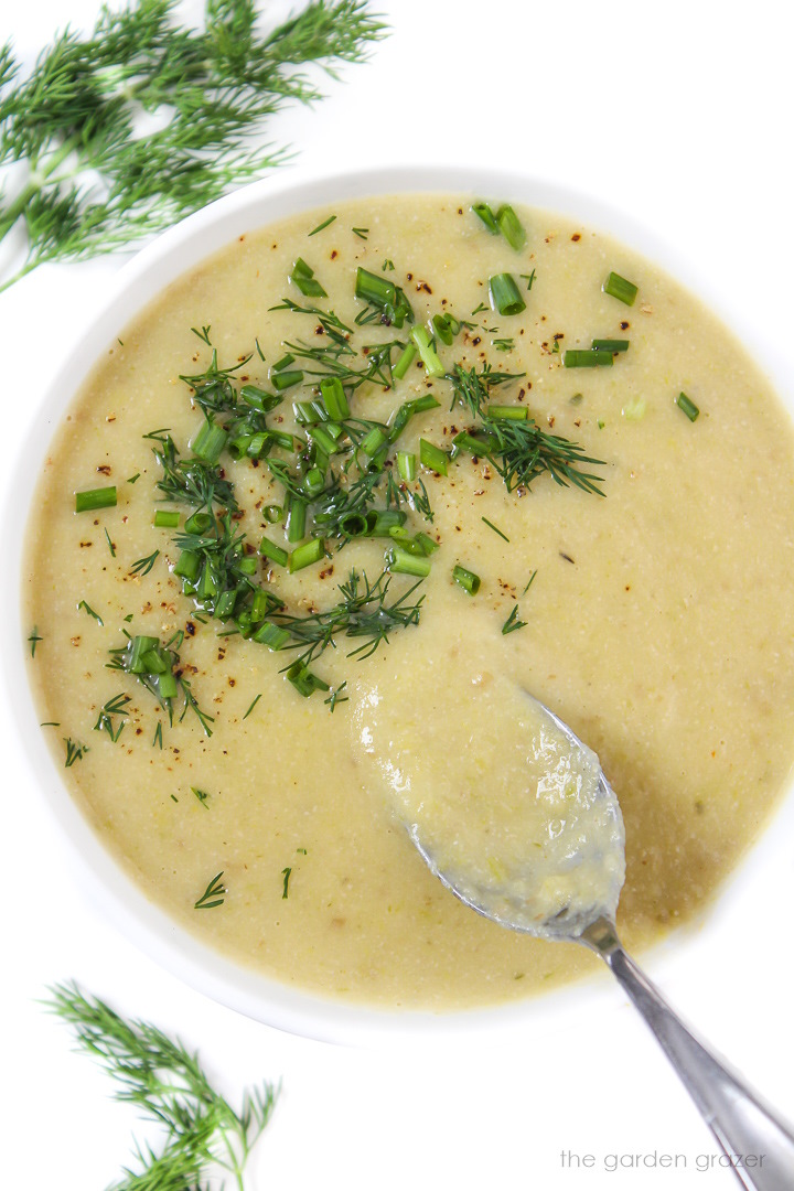 Vegan potato leek soup in a white bowl topped with fresh dill and chives